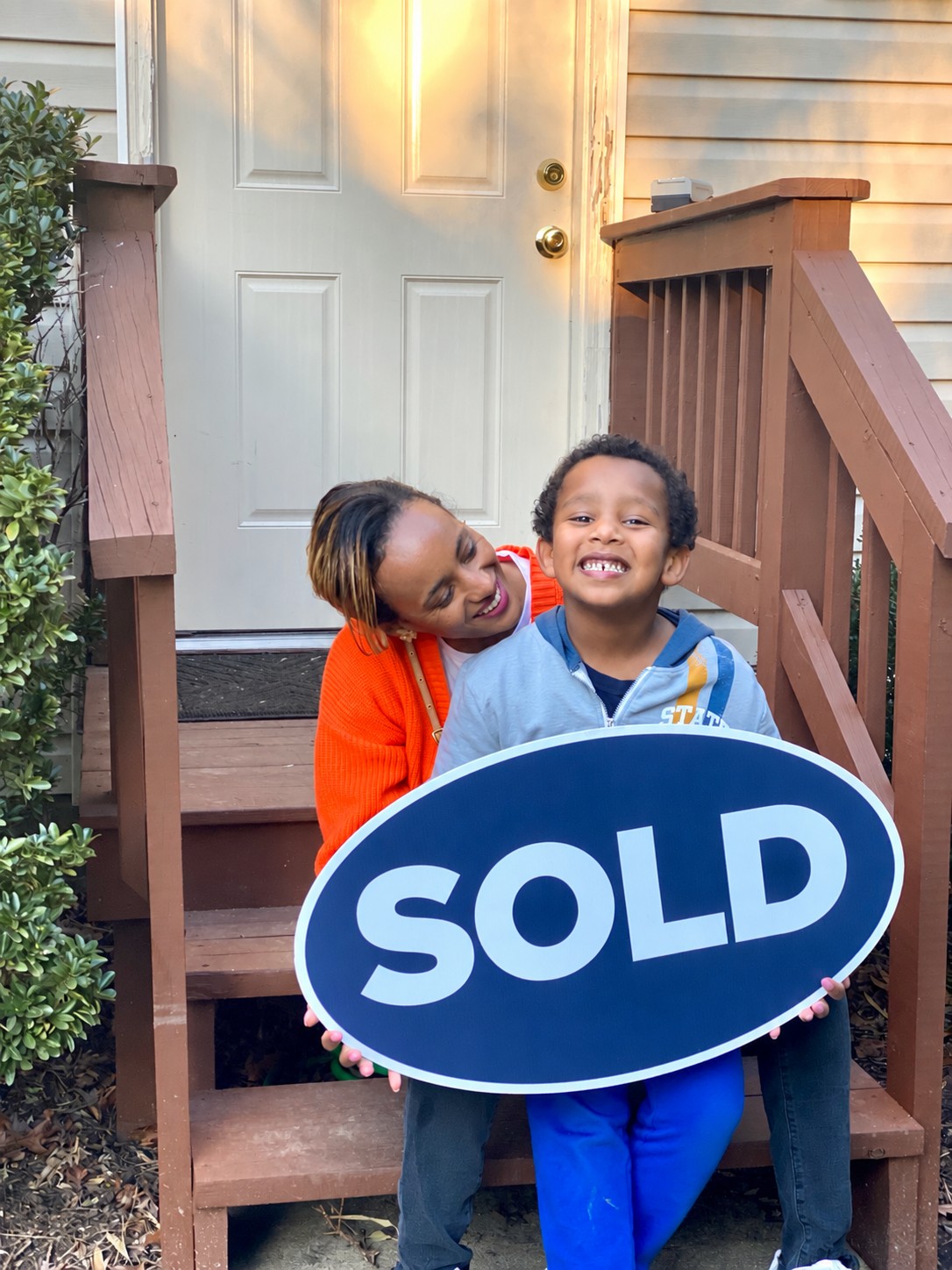 A mother and child celebrating their home purchase with a SOLD sign