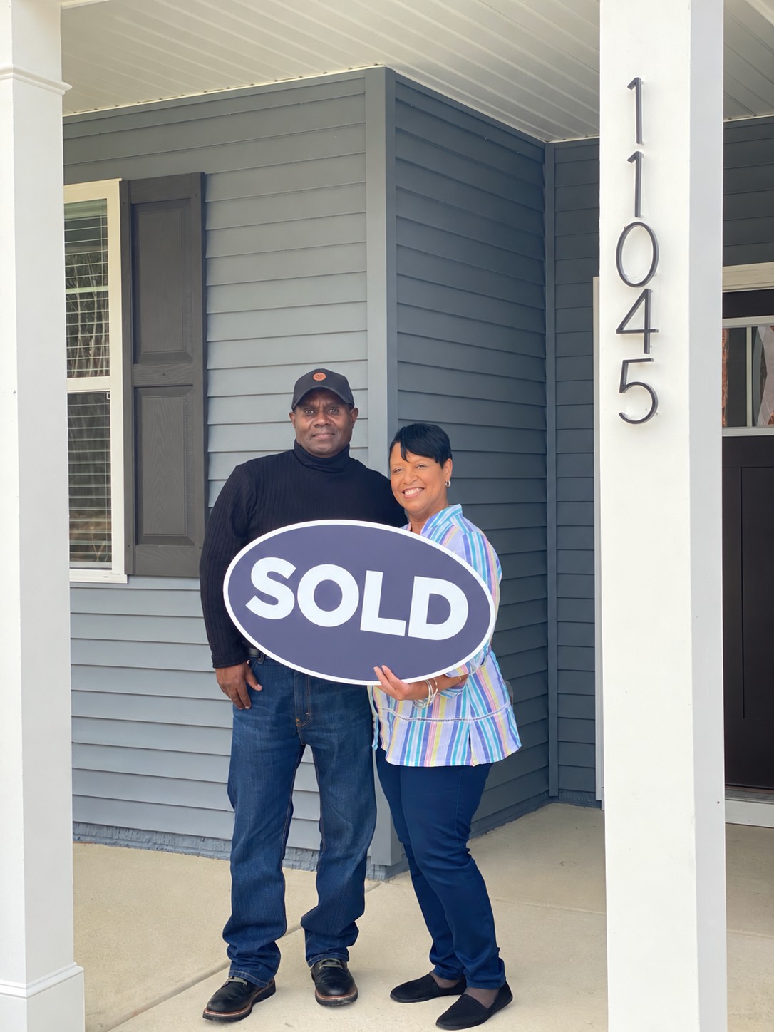 Homebuyers holding their SOLD sign on a porch